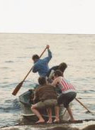 A small square photograph printed on a white page, showing several people standing in shallow water and using oars to propel a small boat or raft.
