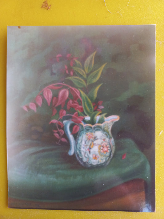 A still life painting of a white floral pitcher with pink leaves and green foliage, resting on a draped green surface against a dark background, displayed on a yellow surface.

