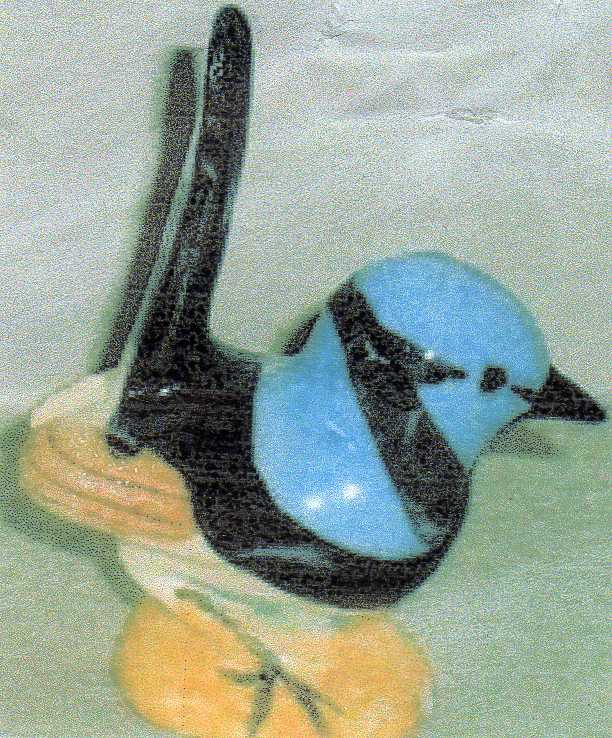 A small bird figurine or ornament with a bright blue head and back, black wings and tail, and pale yellow legs, shown against a soft light green background.

